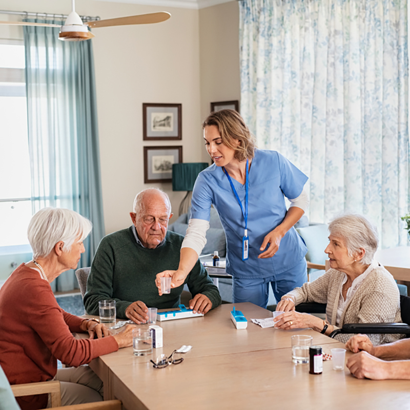 Caregiver,Giving,Medicine,To,Group,Of,Senior,Men,And,Women